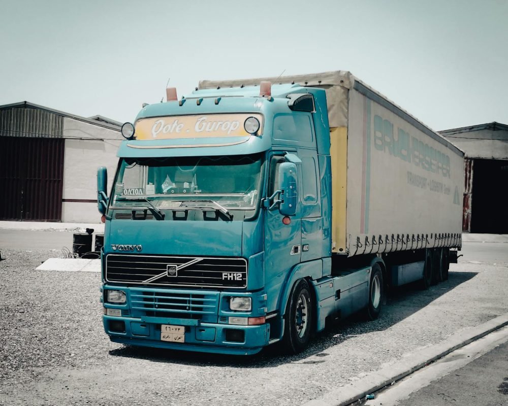 https://www.miteco.gob.es/es/calidad-y-evaluacion-ambiental/temas/gestion-de-residuos/residuos-no-peligrosos.aspx - A blue Volvo truck parked outside a warehouse in an industrial area, daytime scene.